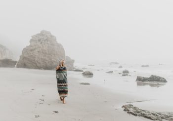 woman wrapped in blanket walking on sandy shore