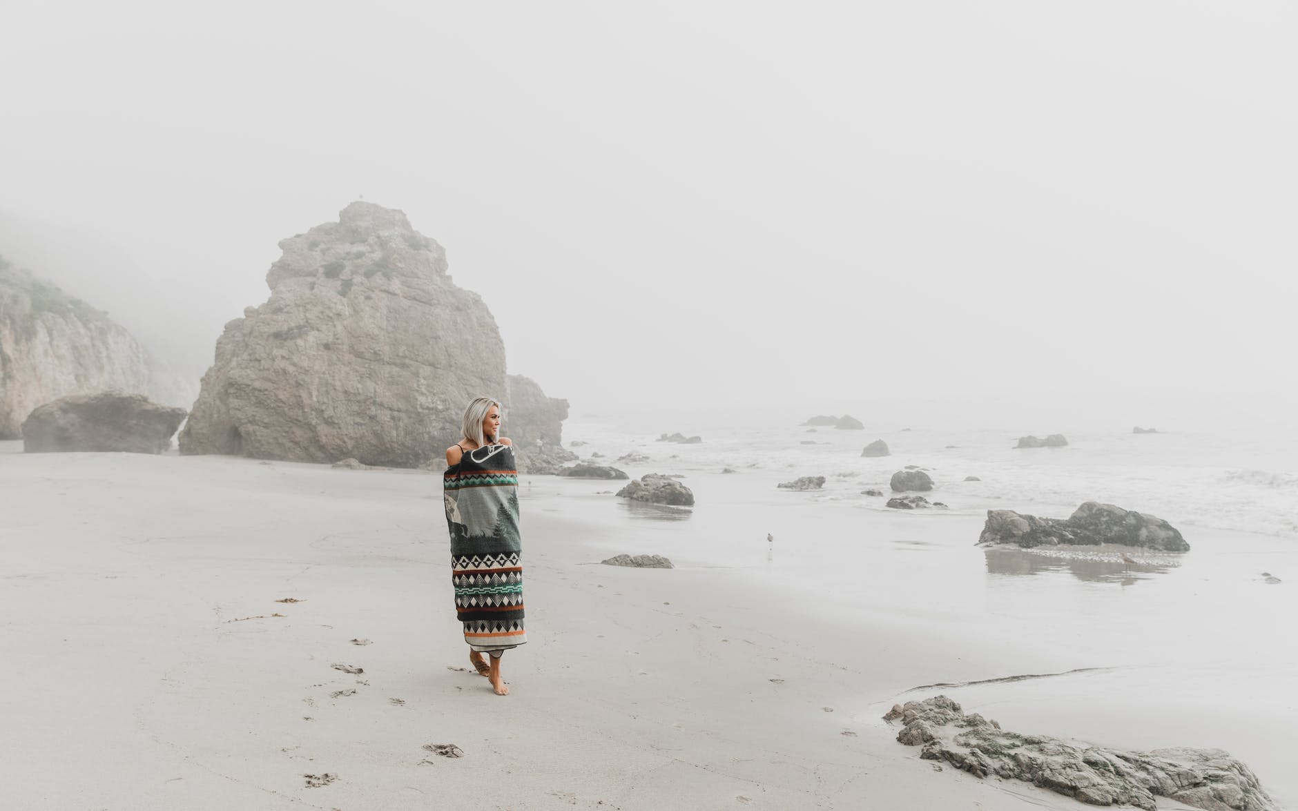 woman wrapped in blanket walking on sandy shore